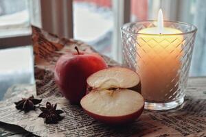 acogedor todavía vida comida fotografía rojo manzanas cortar medio con anís especias en un arte papel siguiente a un vela foto