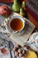 Cozy autumn composition with cup of tea book walnuts and fruits photo