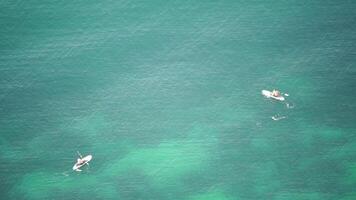 Two people are in the water, one of them is on a surfboard. The water is calm and clear, and the sky is blue. video