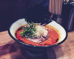 Ramen, a dish with orange broth consisting of pork, vermicelli, half boiled egg, dried seaweed and topped with chopped spring onions and white sesame seeds. photo