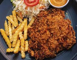 Pork batter with potato sticks and mayonnaise on a black plate photo