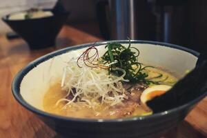 Ramen, a dish with orange broth consisting of pork, vermicelli, half boiled egg, dried seaweed and topped with chopped spring onions and white sesame seeds. photo