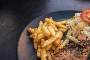 Black pepper marinated chicken fillet with potato sticks on a black plate photo