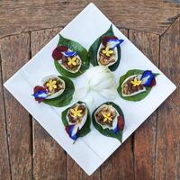 Miang Kham Thai food consists of Cha Phlu leaves, roasted coconut, garlic, nuts, ginger, wrapped in white lotus petals. photo