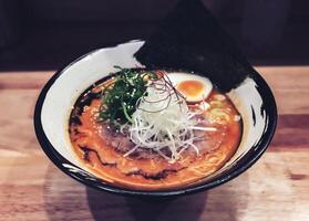 Ramen, a dish with orange broth consisting of pork, vermicelli, half boiled egg, dried seaweed and topped with chopped spring onions and white sesame seeds. photo