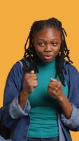 Vertical African american woman jokingly pretending to fight, having friendly confrontation with friend. Young girl mock boxing with mate, holding combat stance, studio background, camera A video