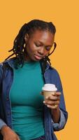 Vertical Tired girl travelling with suitcase, drinking coffee to wake up. Sleepy woman using caffeinated beverage to gain energy, going abroad with briefcase, studio background, camera A video