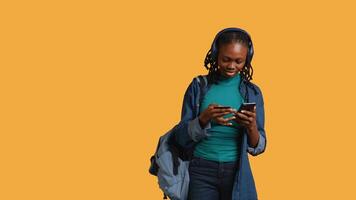 African american teenager adding payment method on website, isolated over studio background. Young girl wearing headphones, doing internet shopping, typing credit card information on phone, camera B video