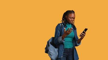 chateado africano americano mulher discutindo com amigos durante teleconferência encontro em Smartphone, estúdio fundo. irritado menina brigando em Móvel telefone ligar com companheiros, Câmera b video