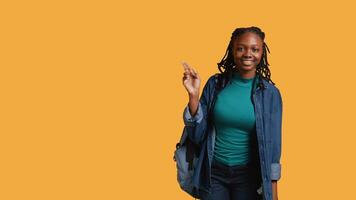 sorridente africano americano aluna às escola levantando braço para responda pergunta, isolado sobre estúdio fundo. alegre menina com mão acima voluntariado para contar professor explicação para pergunta, Câmera b video