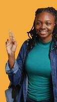 Vertical Smiling african american student at school raising arm to answer question, isolated over studio background. Cheerful girl with hand up volunteering to tell teacher explanation to question, camera A video