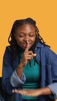 Vertical Stern african american woman doing shushing hand gesturing, irritated by noise, having negative mood. Girl placing finger on lips, doing quiet sign gesture, studio background, camera A video