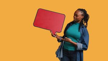 Smiling woman holding red speech bubble sign of empty copy space for message. Joyous person presenting thought bubble cardboard used as promotion concept, isolated over studio background, camera B video