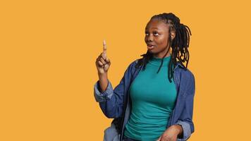 Afrikaanse Amerikaans vrouw richten met vinger in allemaal routebeschrijving, aan het doen reclame, pratend met publiek. jong tiener aan het doen presentatie, tonen kopiëren tekst, studio achtergrond, camera een video