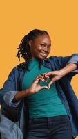 Vertical Portrait of friendly smiling african american woman doing heart symbol shape gesture with hands, being affectionate. Cheerful nurturing person showing love gesturing, studio background, camera B video