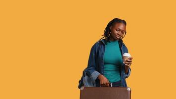 Tired girl travelling with suitcase, drinking coffee to wake up. Sleepy woman using caffeinated beverage to gain energy, going abroad with briefcase, studio background, camera B video