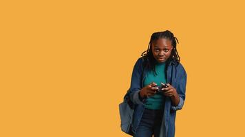 Euphoric african american woman playing intense gaming console game, celebrating win, studio background. Ecstatic young girl using controller, excited after being victorious in game, camera B video