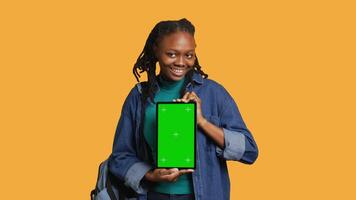 souriant africain américain femme en présentant tablette avec vert écran afficher, isolé plus de studio Contexte. de bonne humeur bipoc la personne création promotion avec chrominance clé appareil, caméra une video