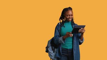 Smiling woman having friendly conversation with friends during teleconference meeting using tablet, studio background. BIPOC person having fun catching up with mates during online call, camera B video