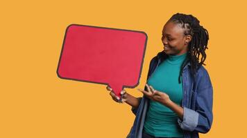 Smiling woman holding red speech bubble sign of empty copy space for message. Joyous person presenting thought bubble cardboard used as promotion concept, isolated over studio background, camera A video