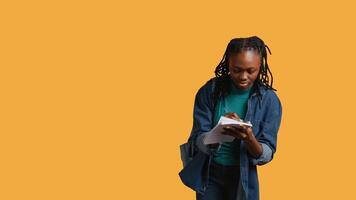 Girl with bad eyesight squinting eyes, trying to read lecture information and take notes at school on notepad, studio background. Student struggling to understand university class material, camera B video