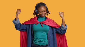 African american superhero with red cape flexing muscles, isolated over studio background. Woman wearing cloak posing as hero in costume kissing biceps, showing strength, camera A video