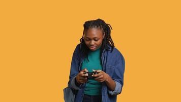 euforisk afrikansk amerikan kvinna spelar intensiv gaming trösta spel, fira vinna, studio bakgrund. extatisk ung flicka använder sig av kontroller, upphetsad efter varelse segrande i spel, kamera en video