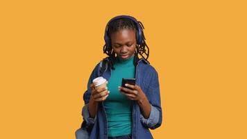 Woman scrolling on smartphone, using phone to check social media feed, drinking coffee. Girl browsing internet websites, enjoying beverage, listening music, isolated over studio background, camera A video