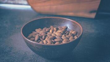 Almonds in a clay plate on the table. Blue tint.16-9 photo