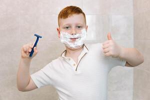 gracioso chico en el bañera con afeitado crema en su cara y afeitado maquinilla de afeitar foto