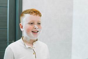 Funny boy in the bath smears his face with shaving cream, the child imitates an adult dad shaves. The boy smeared his cheeks with shaving foam photo