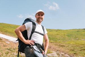 A bearded traveler with a backpack on the top of a mountain. A tourist with a backpack stands against the background of a mountain photo