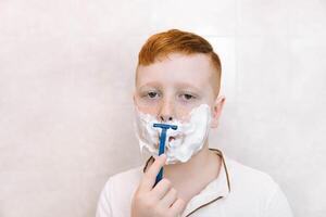 Little boy is shaving his face in the bathroom photo