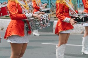 joven muchachas batería en rojo Clásico uniforme a el desfile. calle actuación de festivo marzo de bateristas muchachas en rojo disfraces en ciudad calle foto