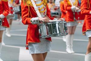 Street performance of festive march of drummers girls in red costumes on city street. Young girls drummer in red vintage uniform at the parade photo