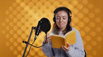 voz ator lê livro enquanto desfrutando café, gravação áudio-livro usando microfone, estúdio fundo. mulher usando microfone e fones de ouvido para produzir digital gravação do romance, bebendo bebida, Câmera b video