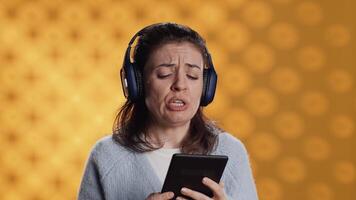 Voice actor frowns while reading ebook, portraying character, studio background. Woman reenacting digital recording of novel, interpreting furious antagonist, reading text from tablet, camera A video