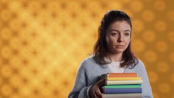 Portrait of smiling woman holding stack of books, doing salutation hand gesture, feeling optimistic. Jolly person with pile of novels raising arm to greet someone, studio background, camera A video