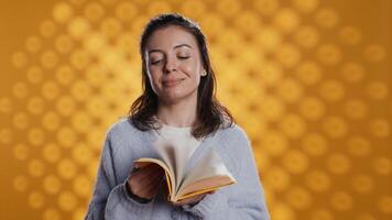 portret van glimlachen vrouw Holding boek ruiken Pagina's overbrengen vreugde van lezing concept, studio achtergrond. vrolijk persoon leuk vinden nieuw roman vers geur, tonen gelukzaligheid, camera b video