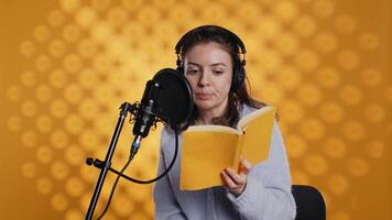 Woman does voiceover reading of book to produce audiobook using dramatic acting. Narrator uses storytelling skills and expressive sounds while producing recording of novel, studio background, camera B video