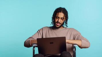 man i rullstol chattar med vän över internet ring upp använder sig av bärbar dator Ansökan. bipoc person med paraplegi chattar med para i konferens uppkopplad möte, studio bakgrund, kamera en video