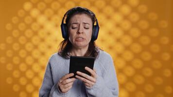 Voice actor frowns while reading ebook, portraying character, studio background. Woman reenacting digital recording of novel, interpreting furious antagonist, reading text from tablet, camera B video