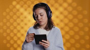 kvinna läsning ebook på e-läsare och lyssnande musik köp av böcker uppkopplad. person med läsplatta ser till köpa digital ny med kreditera kort, hörsel låtar i hörlurar, studio bakgrund, kamera b video