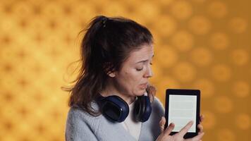 ritratto di sorridente donna mostrando ebook lettore per interessato clienti, fare annuncio. radiante persona fare promozione per lettura tavoletta, mostrando caratteristiche, studio sfondo, telecamera un' video