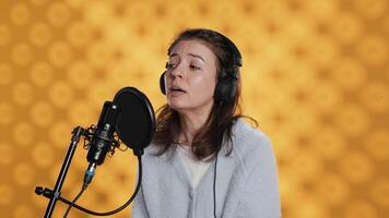 Voice actor reading book, recording for audiobook production using microphone and headset, studio background. Person using mic and headphones to produce digital recording of novel, camera A video