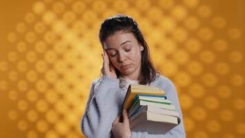 Woman with worried facial expression feeling migraine pain, carrying books for school exam, studio background. Stressed student with textbooks suffering headache from too much homework, camera B video