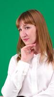 Emotions of a young happy red-haired girl putting her hand on her chin and thinking, On a green background vertical video