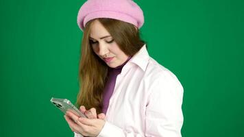 un' bellissimo francese donna nel un' rosa berretto gioca, testi, fa acquisti su il Telefono, smartphone. su un' verde sfondo video