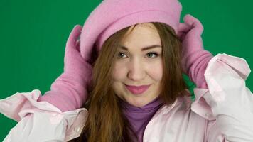 A beautiful, stylish French woman in pink gloves and a pink beret adjusts her beret, smiles, looks into the frame. On a green background video