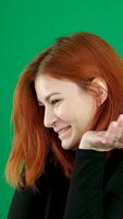 The red-haired girl smiles, then turns and looks seriously at the camera. On a green background, Vertical video